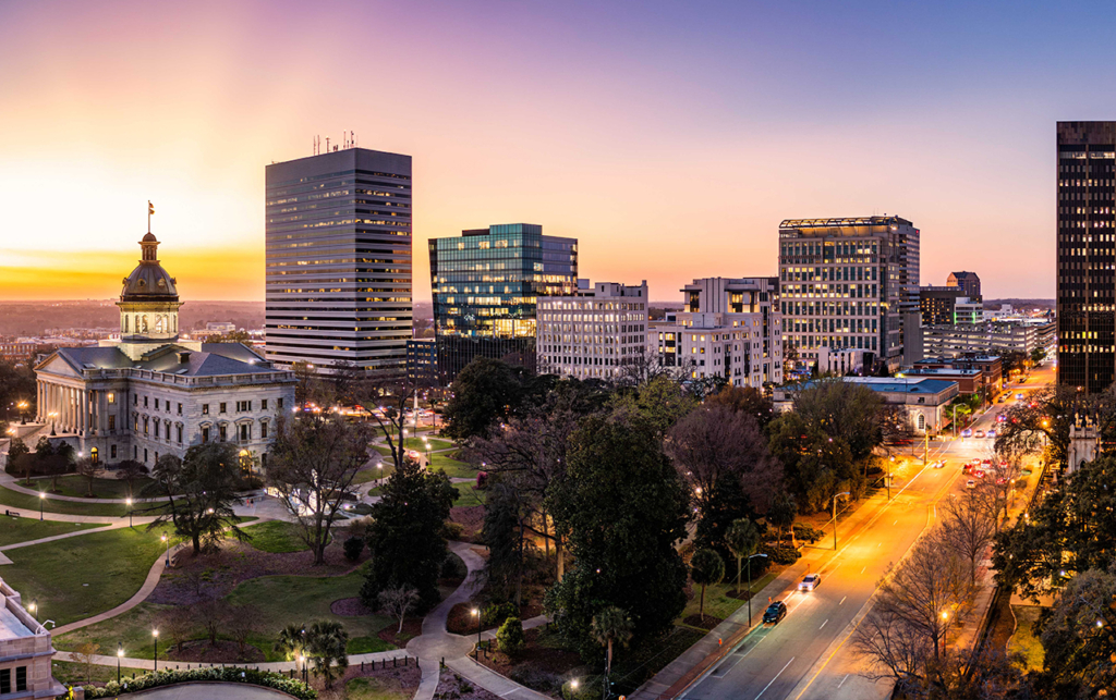 Downtown Columbia, SC skyline at sunset, featuring the South Carolina State House and modern city buildings.